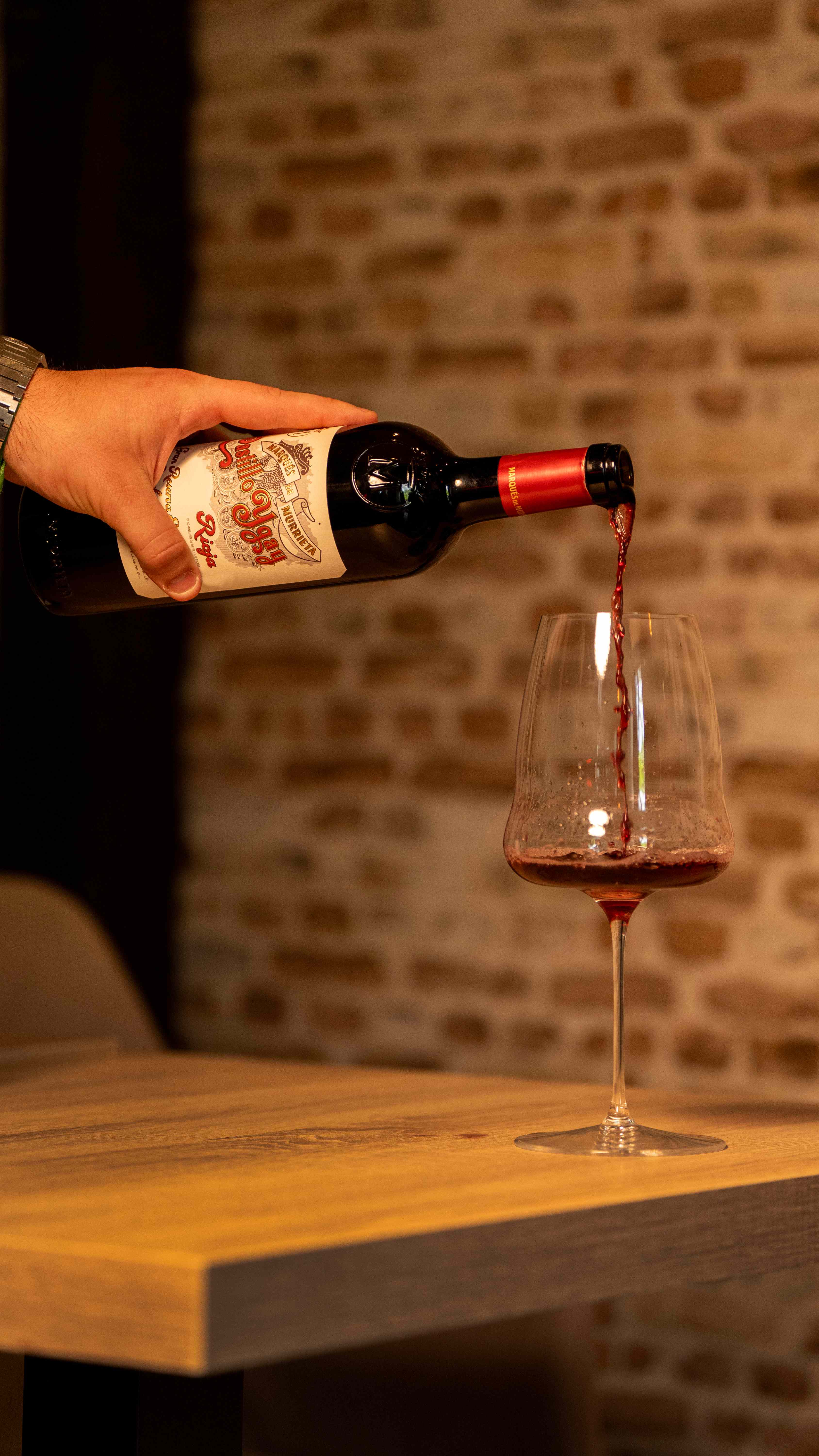 Servicio de vino tinto en copa junto a la pared de ladrillo en Vino y Verás